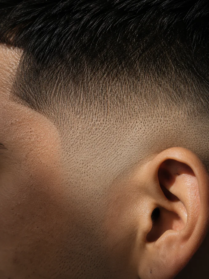 Close detail of a mid drop fade bald fade blend near the ear